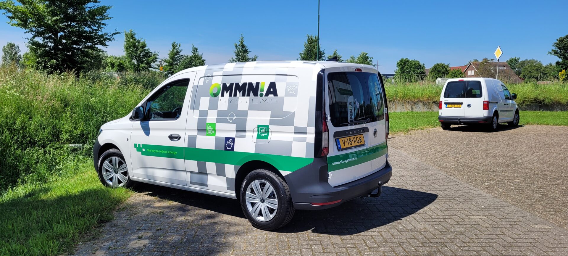 Bedrijfswagen van Ommnia Systems geparkeerd in een groene omgeving, voorzien van branding en slogan "the key to reduce energy".